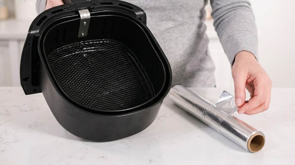 Air fryer basket lined with foil next to parchment paper alternative on kitchen counter
