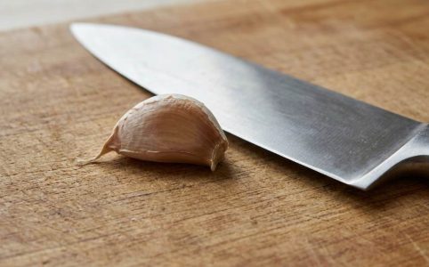 Person mincing fresh garlic cloves on a wooden cutting board with a chef's knife
