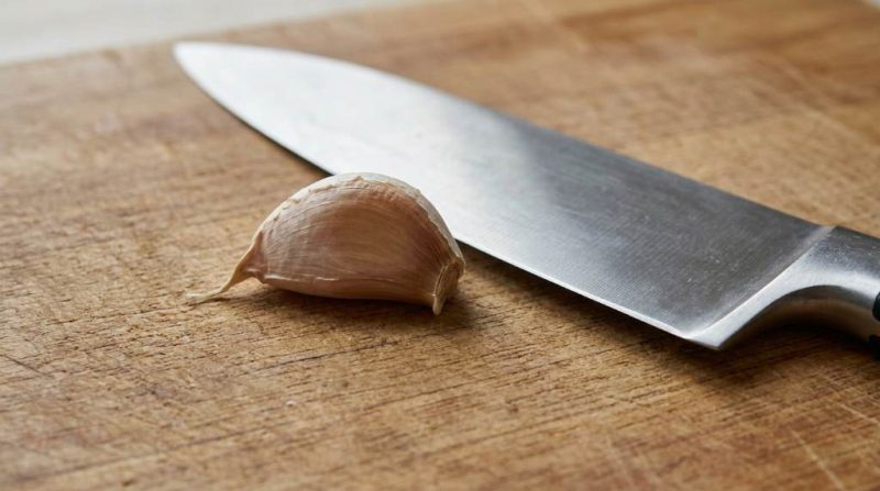 Person mincing fresh garlic cloves on a wooden cutting board with a chef's knife