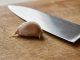 Person mincing fresh garlic cloves on a wooden cutting board with a chef's knife