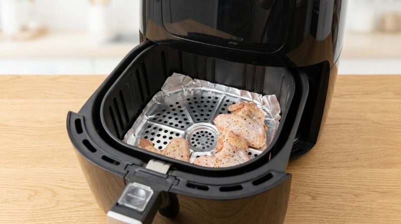 Person placing aluminum foil in an air fryer basket before adding chicken wings