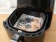 Person placing aluminum foil in an air fryer basket before adding chicken wings