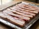 Crispy bacon strips cooking on a baking sheet inside an oven